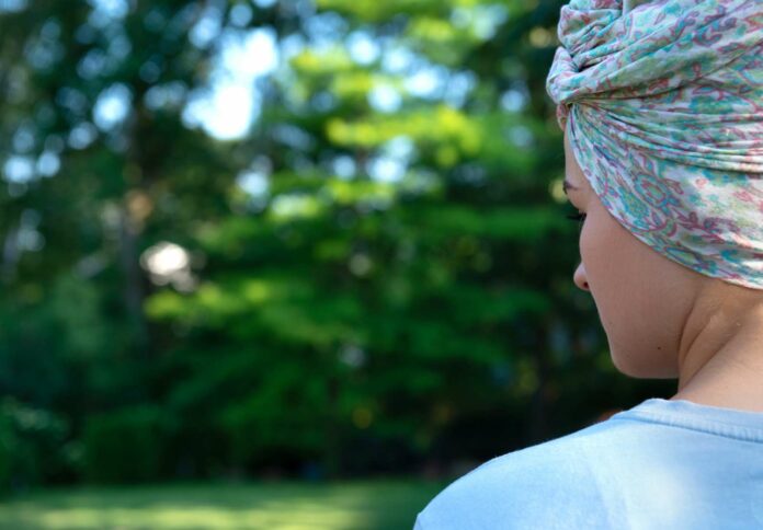 Bild zeigt eine junge Frau mit einem bunten Kopftuch, die auf eine Wiese schaut.
