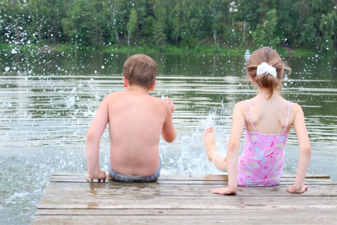 Zwei Kinder planschen im Wasser vom Steg aus