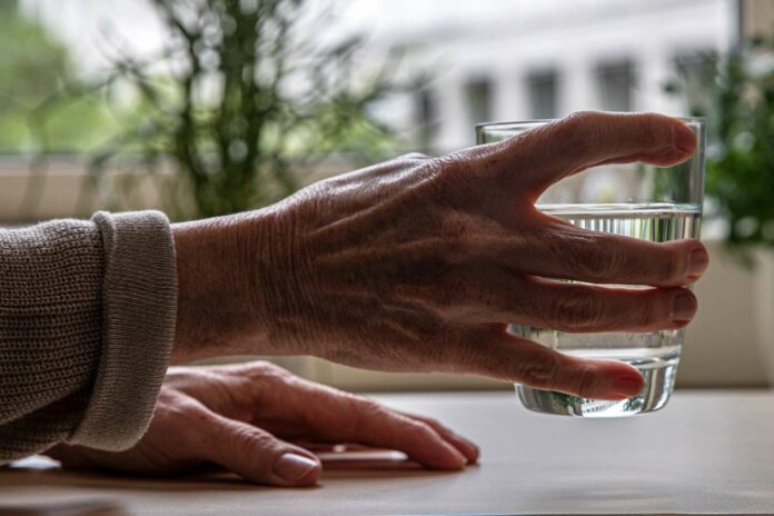 Ältere Person greift Wasserglas zum trinken