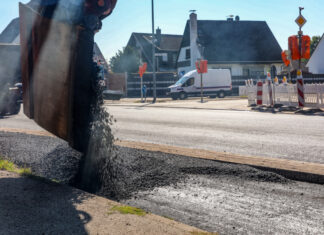Update zur Fahrbahnsanierung am Reuterdamm Baggerschaufel schüttet Teer in eine Baustelle