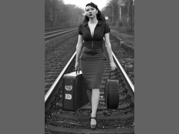 Themenfoto: Frau mit Koffern spaziert auf Bahngleisen