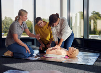 Erste Hilfe mit Selbstschutzinhalten Eine Erste-Hilfe-Ausbilderin der Johanniter erklärt zwei Kursteilnehmerinnen die Herz-Lungen-Wiederbelebung mithilfe einer Reanimationspuppe.