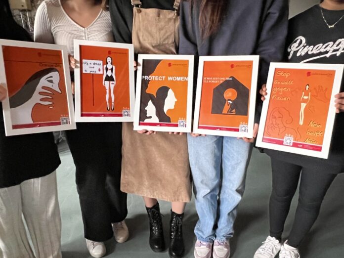 Fünf Schülerinnen des Wahlpflichtkurses „Logo und Design“ der IGS Süd präsentieren ihre Plakate, die sie im Rahmen der Kampagne zum „Orange Day“ gestaltet haben.