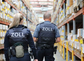 152 Verstöße gegen den Mindestlohn aufgedeckt – Kurierdienst-Inhaber muss über 200.000 Euro Strafe zahlen Zöllner vor Hochregalen mit Paketen