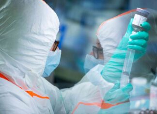 Mit Gentherapie gegen die Bluterkrankheit Eine Frau mit Mundschutz und spezieller Kleidung hält Utensilien zur Herstellung eines Medikaments in den Händen.