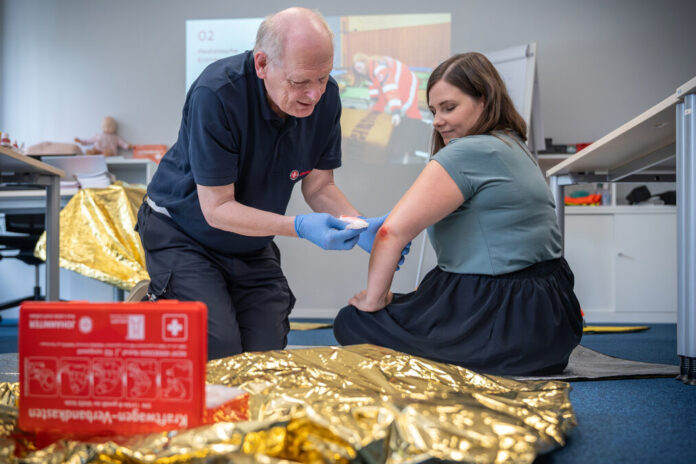 Ein Erste Hilfe-Trainer zeigt am Beispiel einer Teilnehmerin in einem Erste Hilfe-Kurs, wie man einen Verband am Ellenbogen anlegt.